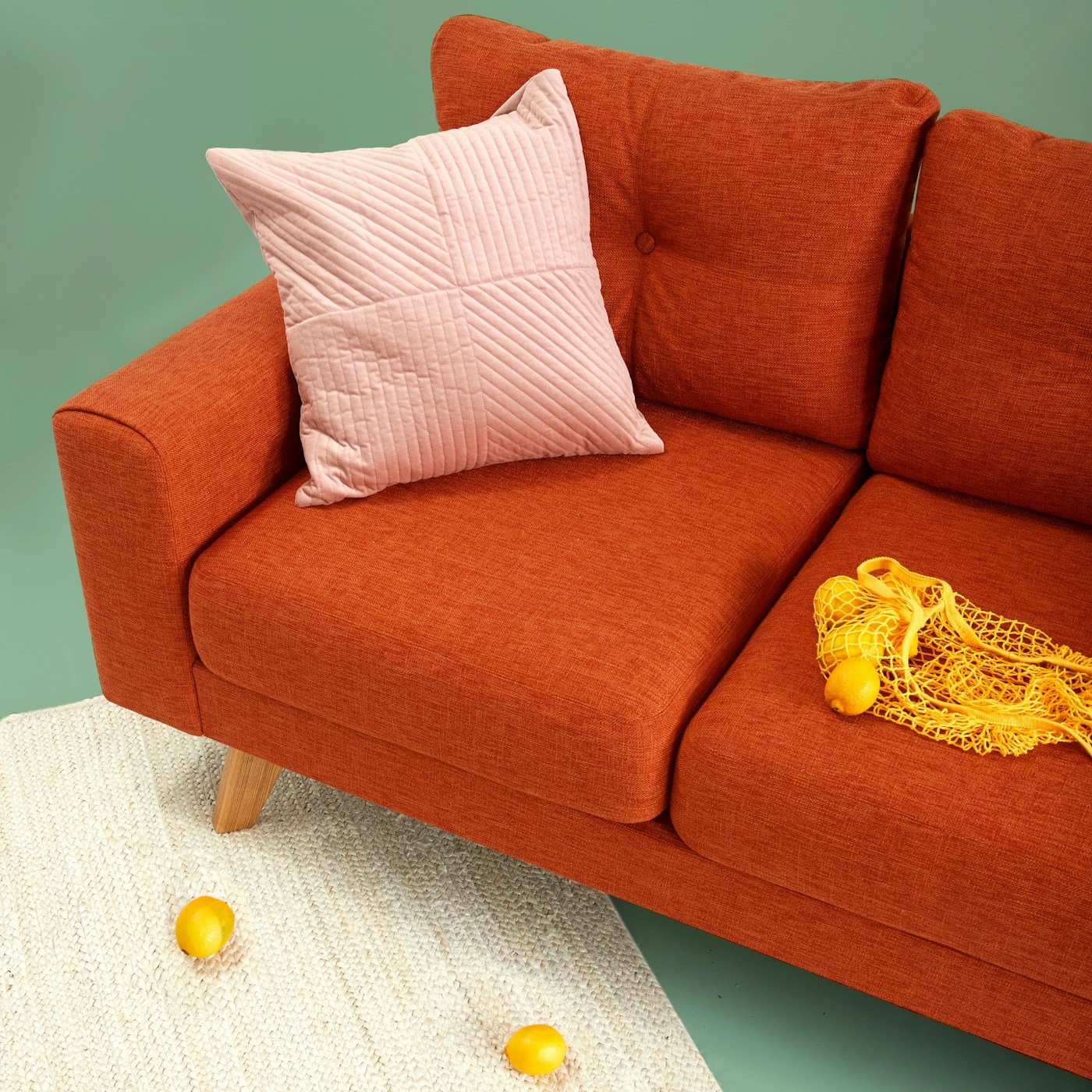 An upholstered rust sofa with a quilted cushion and woven rug
